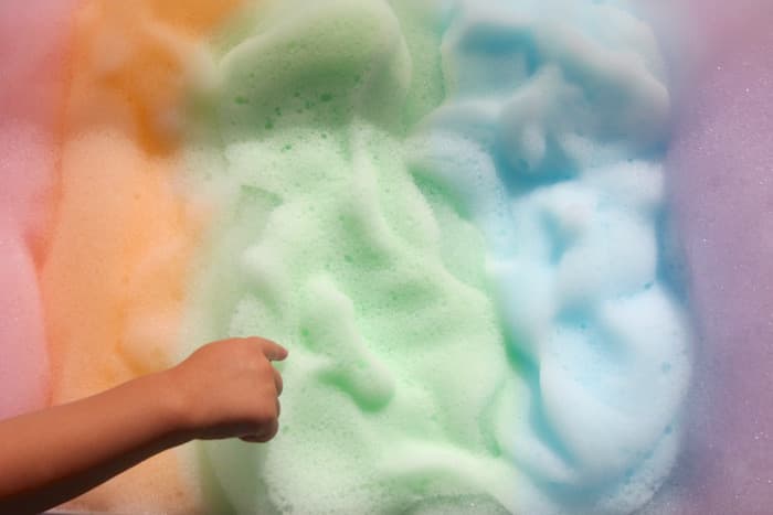 Foam with different colours like a rainbow and a child is touching it