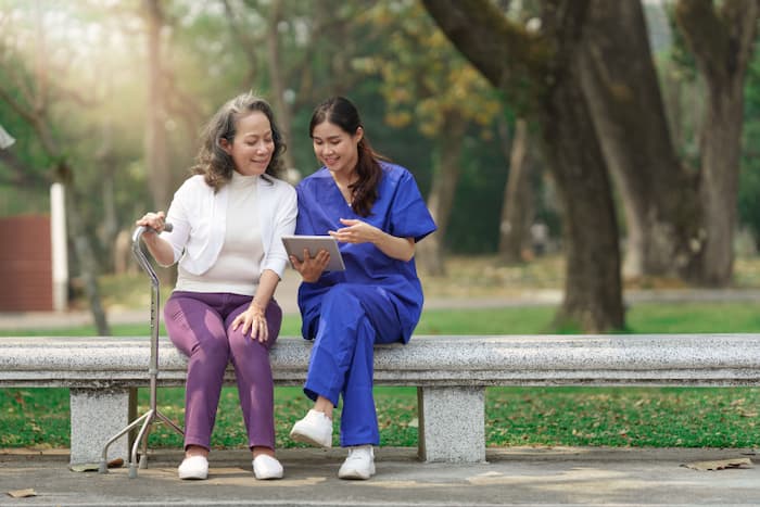 An older woman sitting on a bench next to her therapist and looking at a tablet