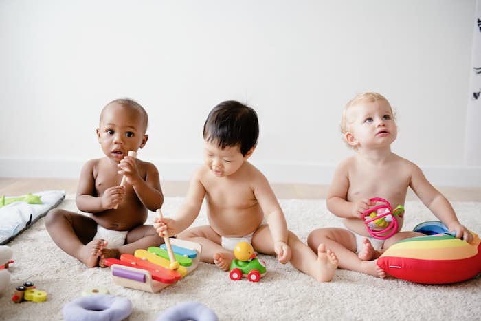Τρια μωρά κάθονται στο πάτωμα και παίζουν διαφορετικά παιχνίδια